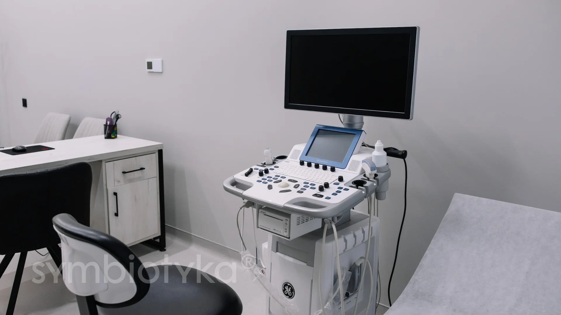 Ultrasound machine with monitor and control panel in a medical examination room.