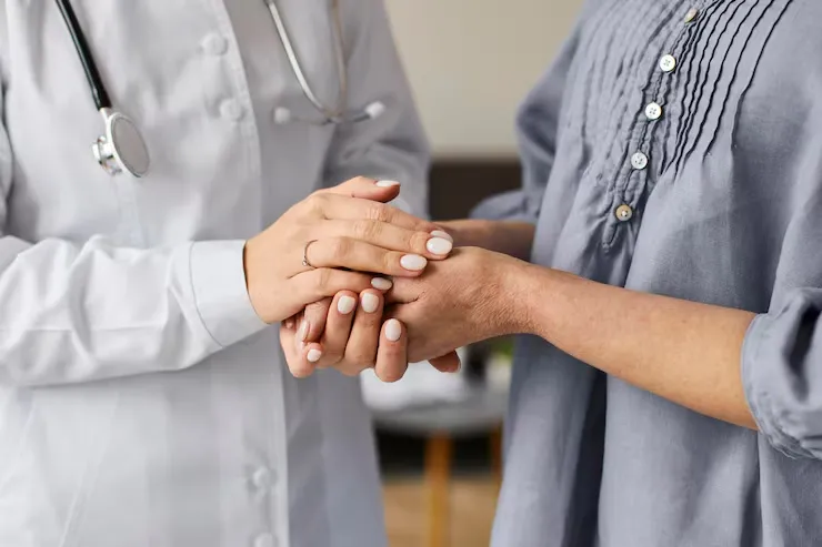 Healthcare professional in white coat holding the hands of a patient wearing a gray shirt in a comforting gesture.