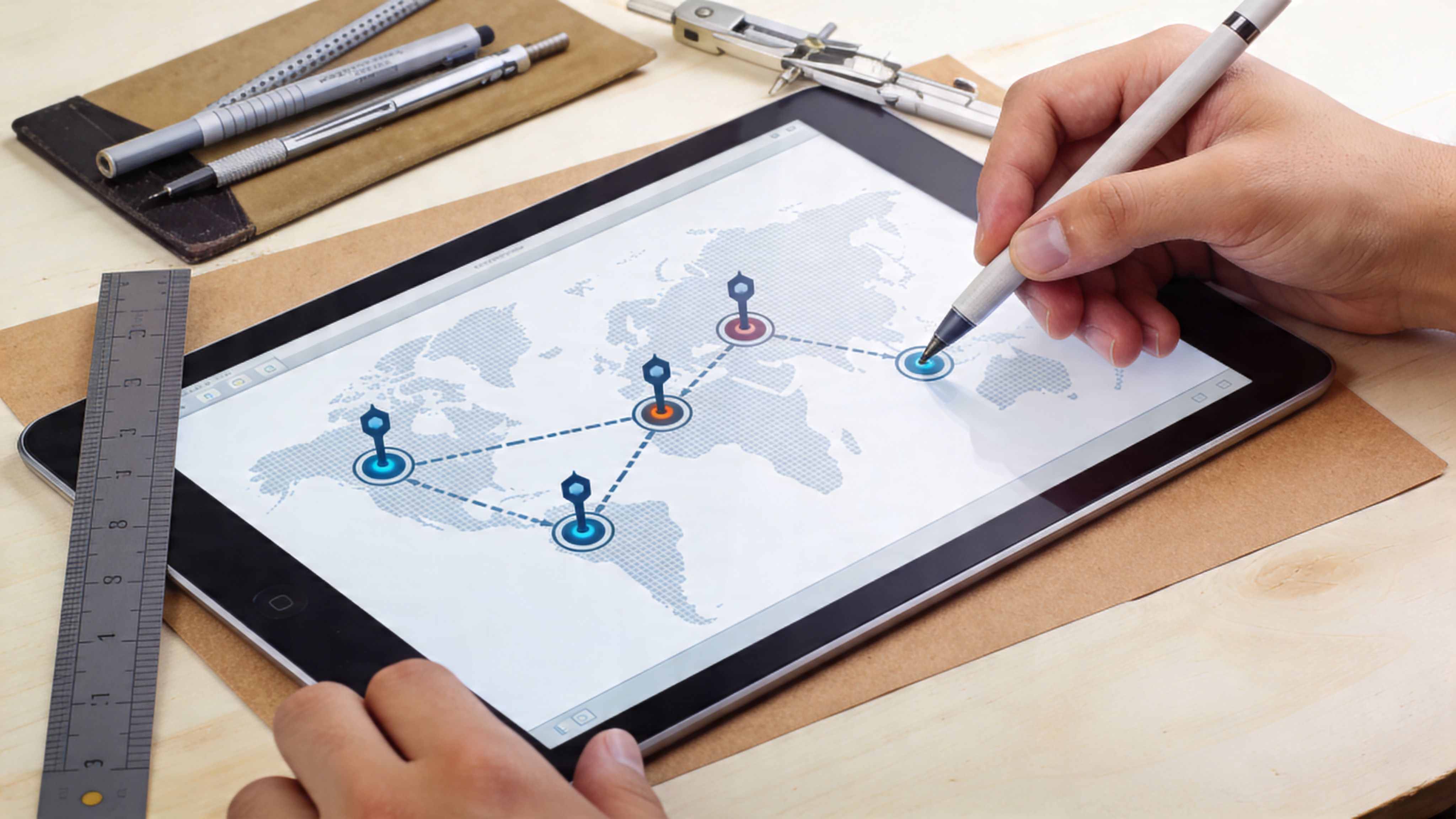 Una mano usa un lápiz táctil sobre una tableta mostrando un mapa mundial con nodos de ubicación conectados.