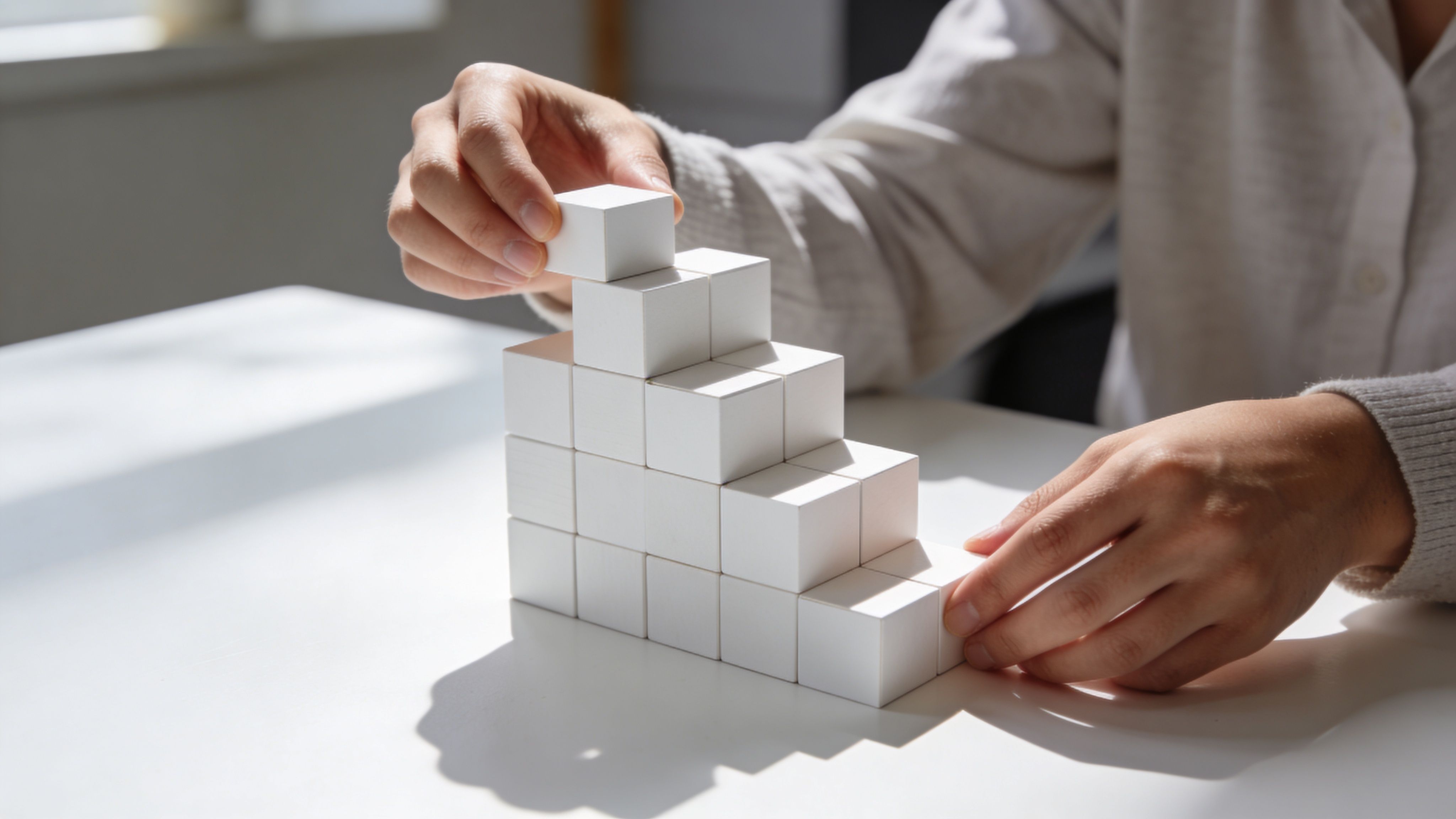 Una persona coloca cuidadosamente un cubo blanco en una estructura en forma de escalera sobre una mesa.