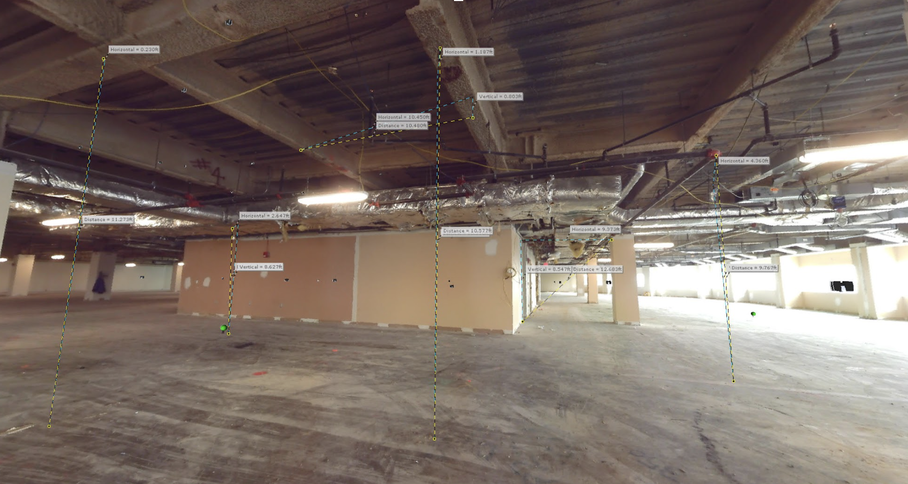 A spacious, vacant room filled with numerous wires and pipes running along the walls and ceiling.