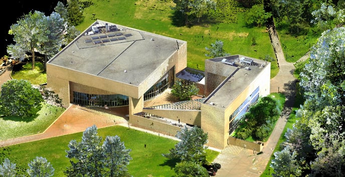 Aerial view of a building surrounded by lush trees and green grass, showcasing a harmonious blend of nature and architecture.