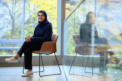 Woman smiling and sitting in front of glass windows.