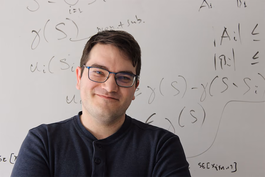Headshot of Gabriele Farina in front of a whiteboard with equations