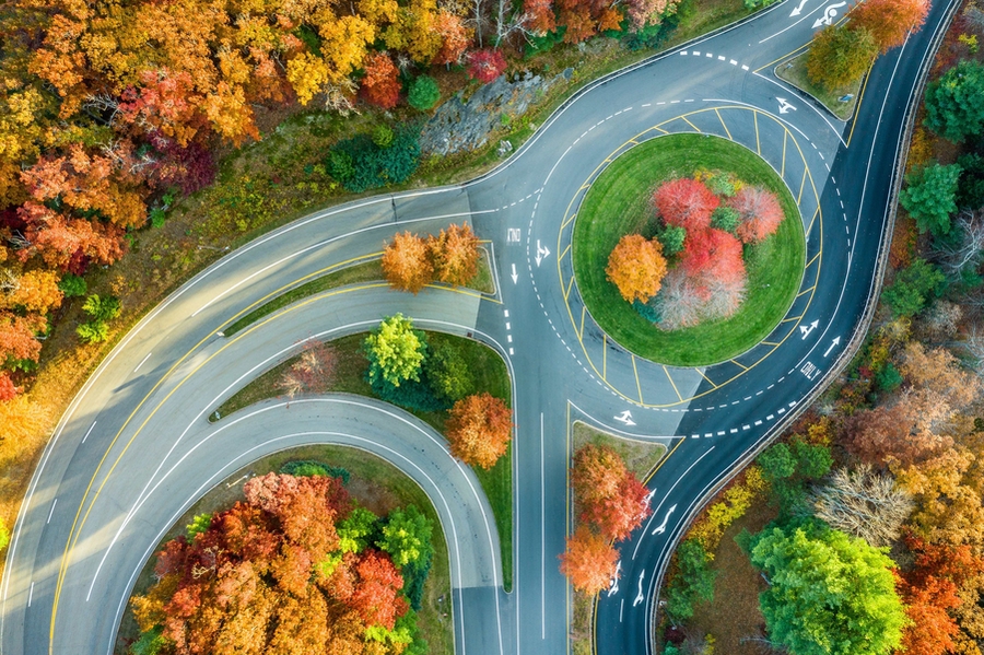 Aerial overhead view of several roadways converging into and separating out from a rotary amidst fall foliage.