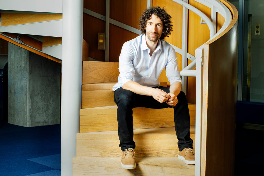 Guy Bresler sits on a wooden spiral staircase inside the Stata Center.