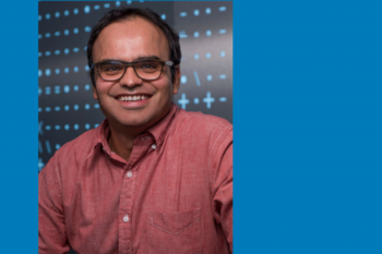 a photo of Devavrat Shah in front of an LED screen with blue icons & symbols