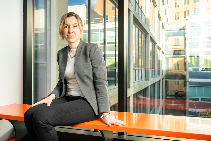 a photo of Asu Ozdaglar sitting on an orange bench in front of a window