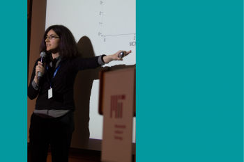 an image of Tamara Broderick giving a talk with a microphone in her hand as she points to a presentation image