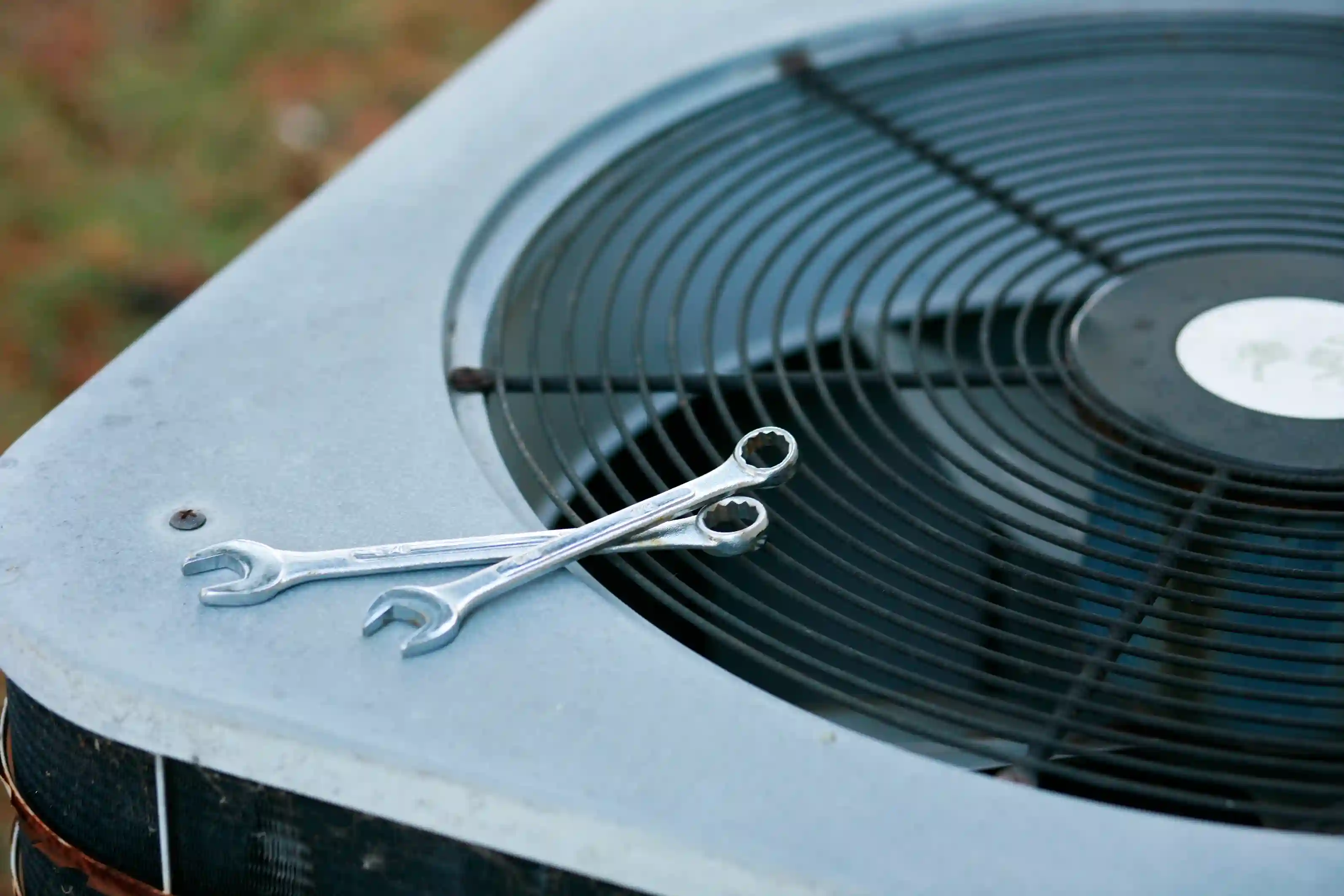 Two wrenches crossed on top of outdoor air conditioning unit with protective fan grille
