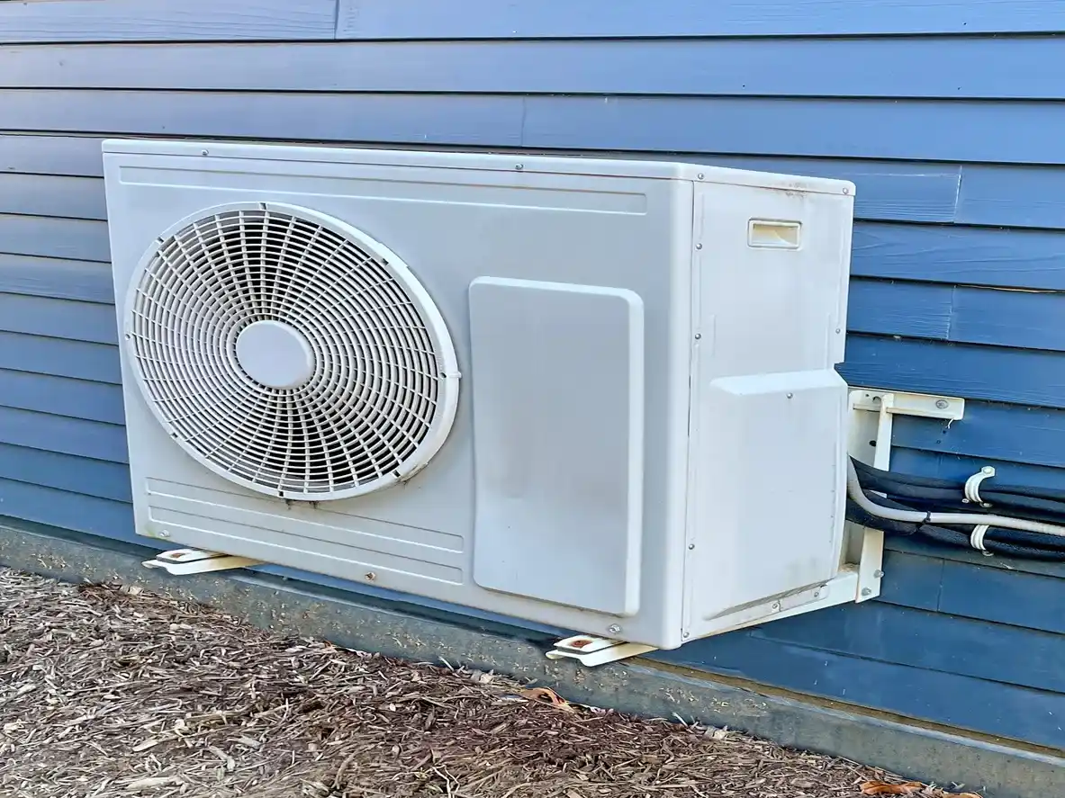 White outdoor air conditioning unit on blue siding wall with large fan and connected cables