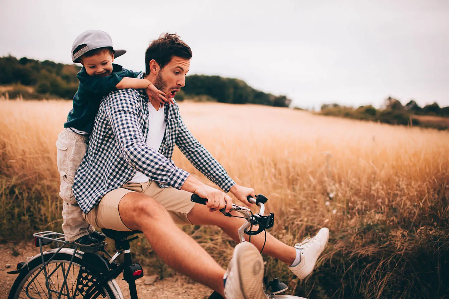 Vater mit Sohn haben Spaß auf einem Fahrrad in einem Weizenfeld