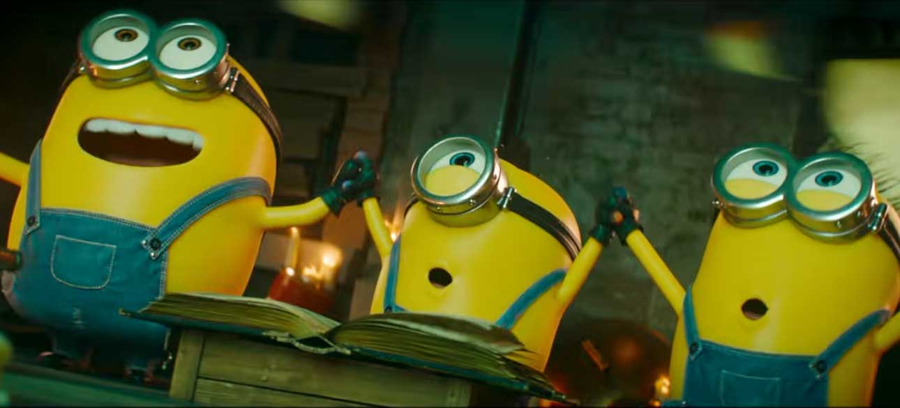 Drei Minions halten die Hände, während sie vor einem offenen Buch stehen.