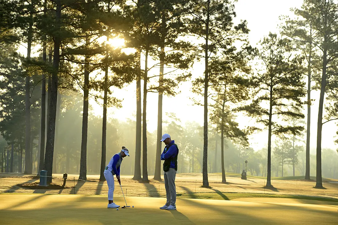 Woman and coach working on golf swing with tall trees in the background