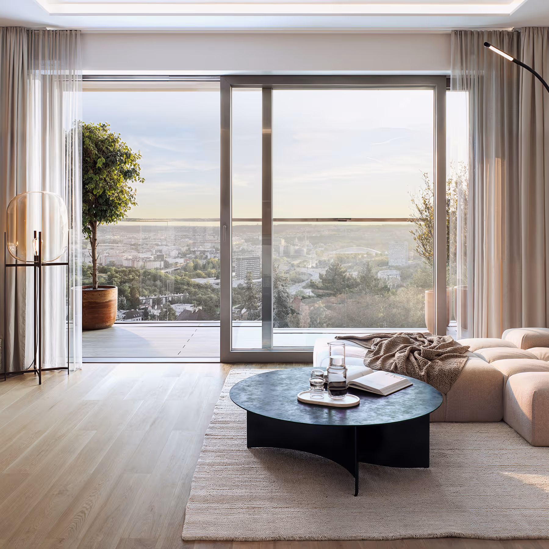 Moderní obývací pokoj s nízkým černým kulatým stolkem, krémovou pohovkou a velkými posuvnými dveřmi s výhledem na město a přírodu.