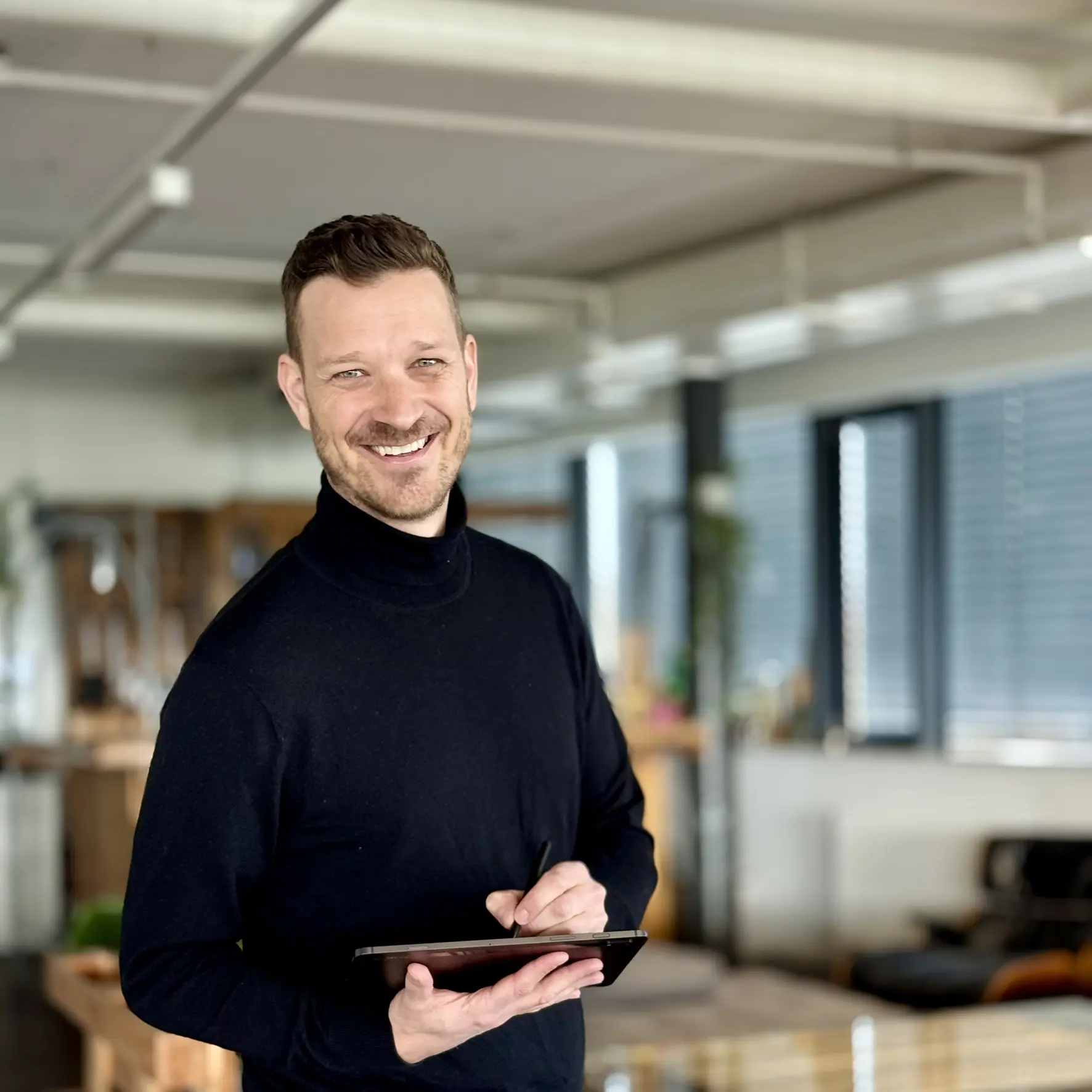 Photo Manuel Zingg, directeur d'homesecurity, cheveux bruns courts et pull à col roulé noir, en arrière-plan une étagère avec des livres et des plantes.