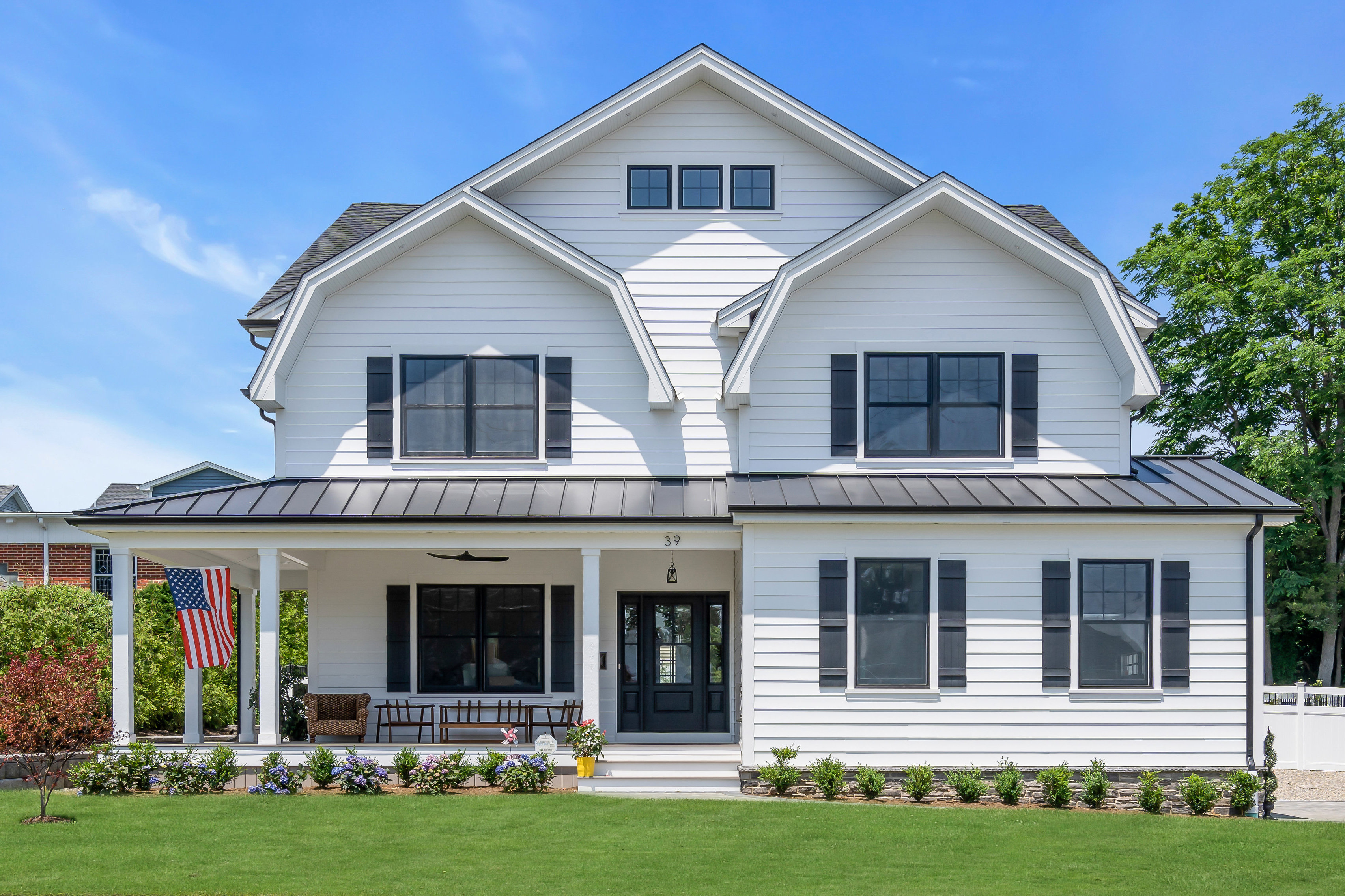White modern farmhouse with black shutters, metal roof, front porch, and an American flag done J.A.Y. Construction.