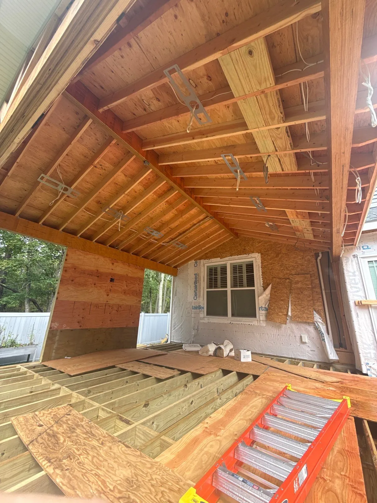 Covered deck under construction by J.A.Y. Construction in Toms River, NJ, showing exposed roof framing, electrical rough-in, and open deck joists before the ceiling and decking are installed.