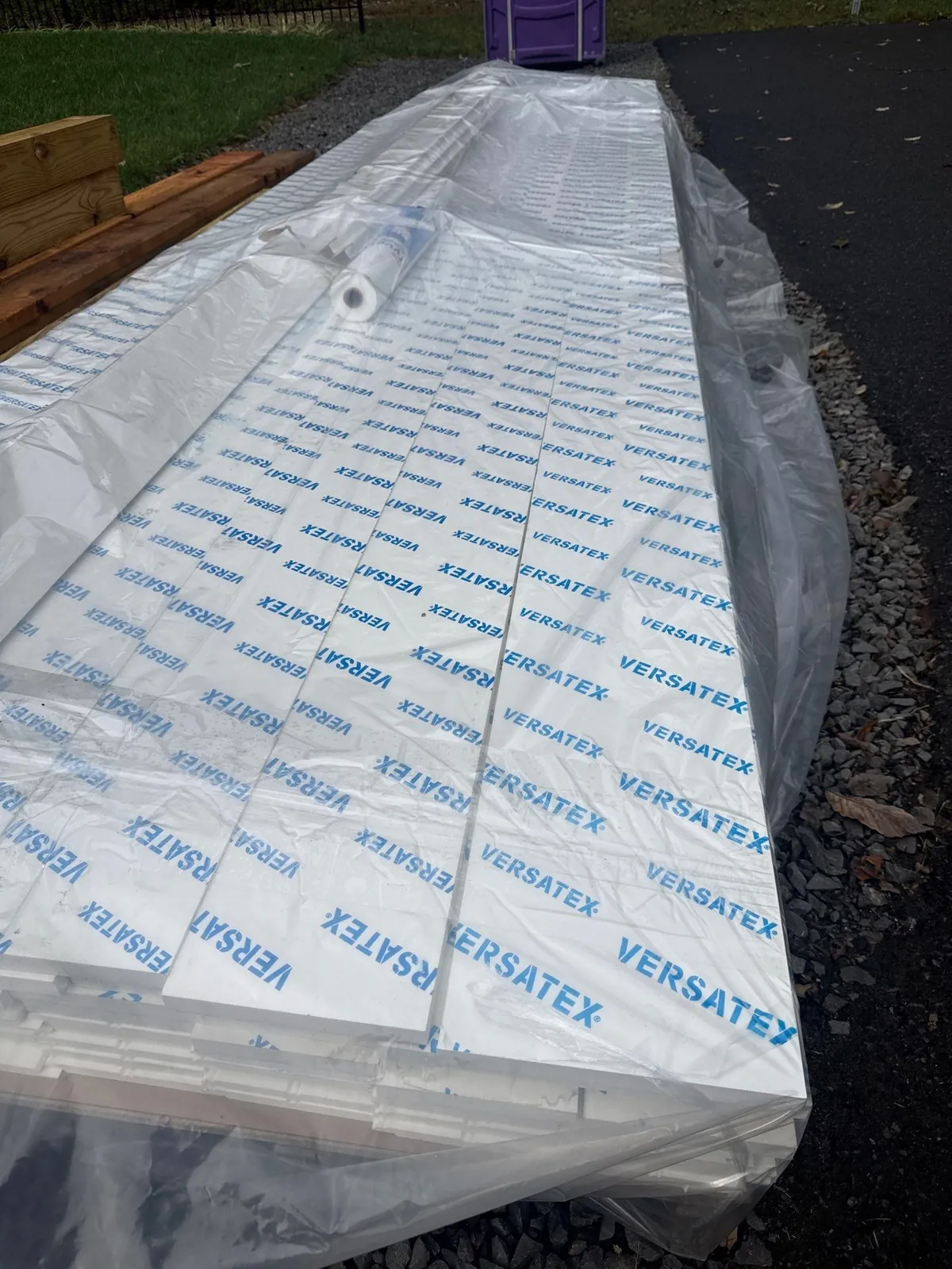 Wrapped VERSATEX boards staged beside lumber for a covered deck project by J.A.Y. Construction.