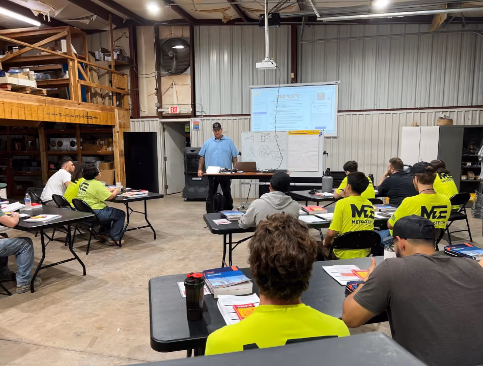 Instructor teaching in a workshop with students wearing bright yellow Metrotech shirts seated at tables.