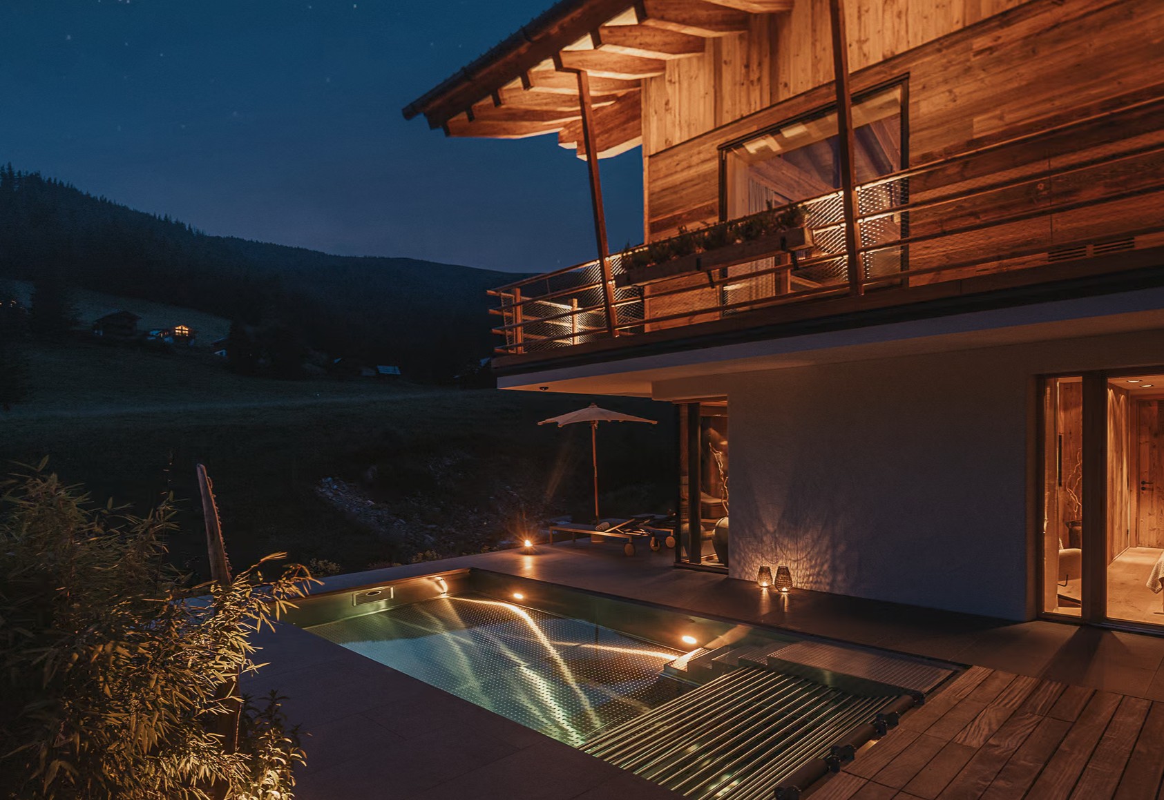 Beheizter Außenpool des CHALET FALK bei Nacht in St. Oswald, Kärnten, Luxus-Berghütte mit beleuchteter Terrasse und Bergkulisse