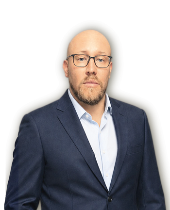Bald man with glasses and beard wearing a navy suit and light blue shirt, looking at the camera.