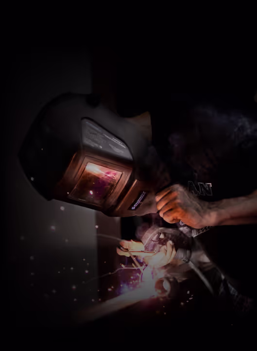 A person in a welding mask working with a welding machine