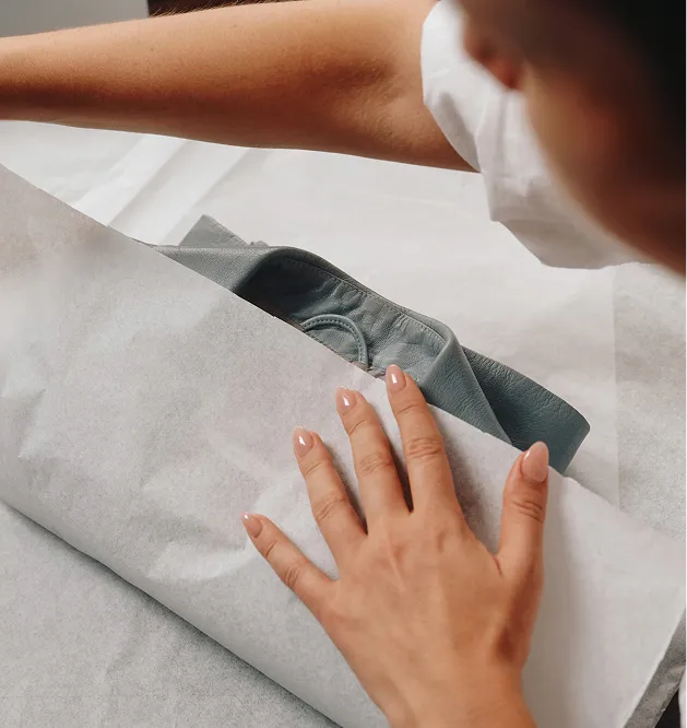 Hands wrapping a leather bag in tissue paper before shipping