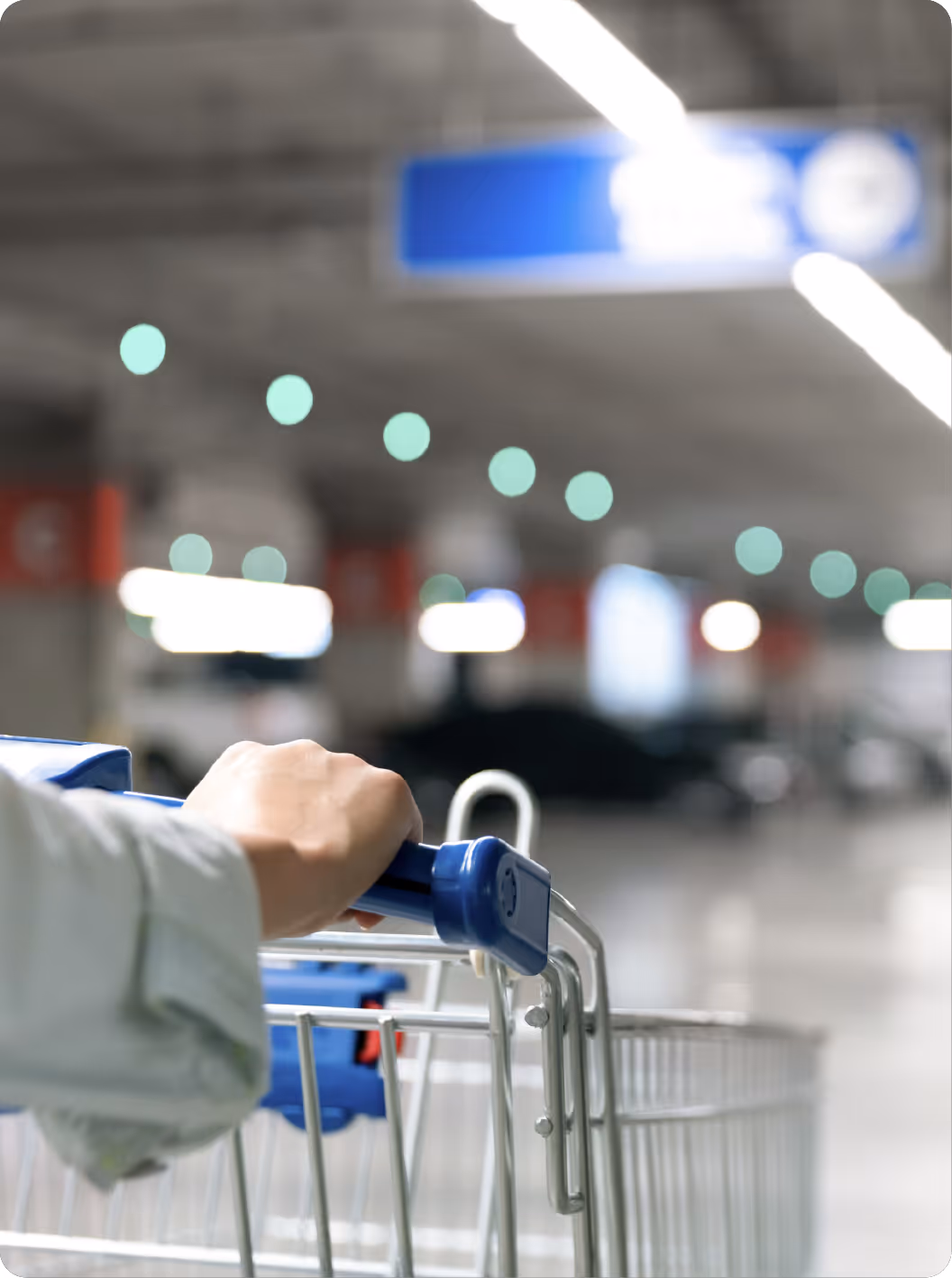 Personne poussant un caddie avec une poignée bleue dans un parking couvert flou.