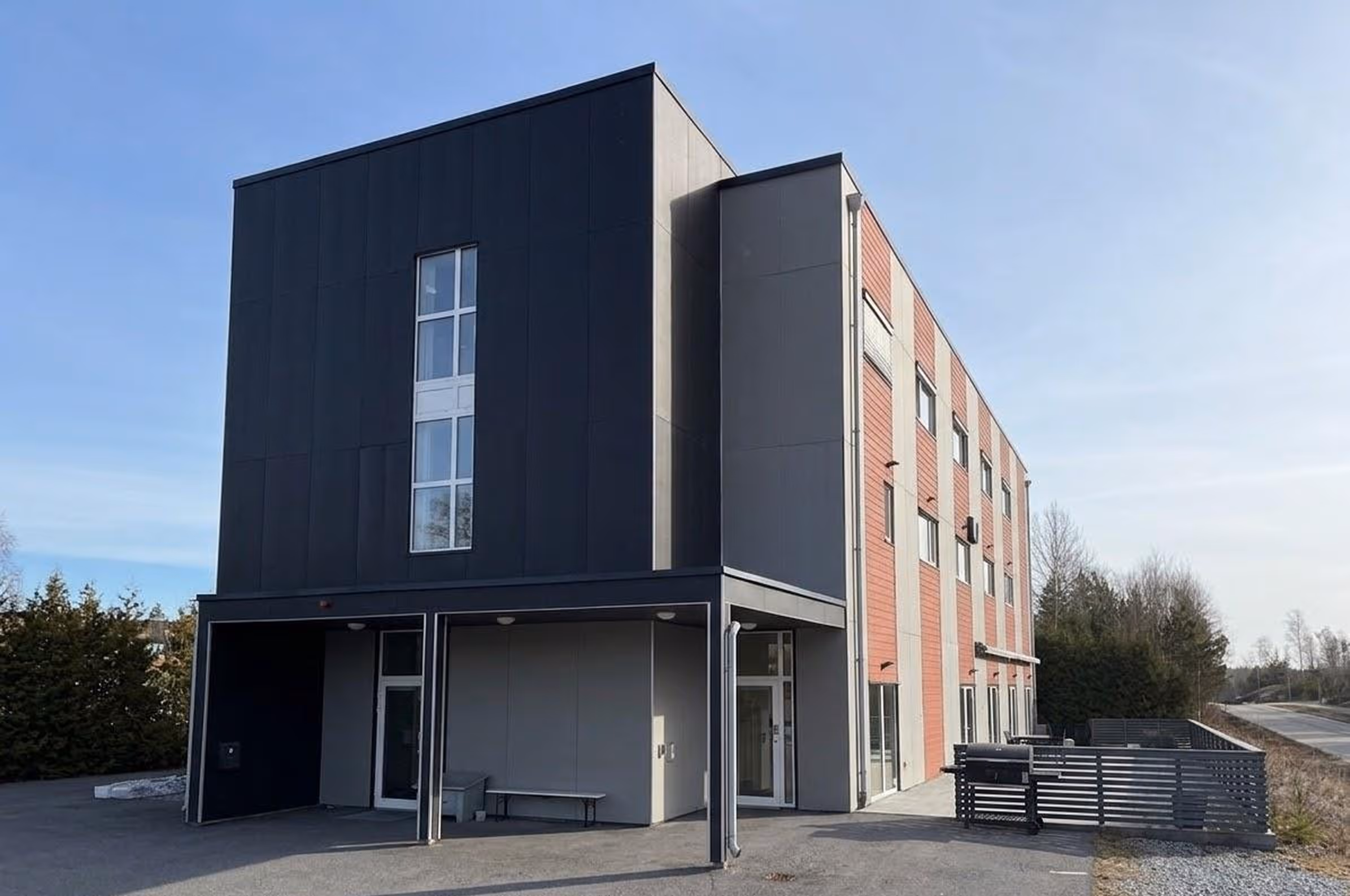 Modern Omvida care facility building with dark and red-brick facade, featuring large windows and a covered entrance