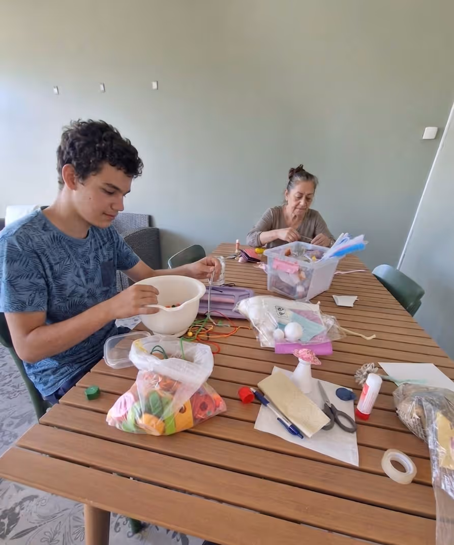 Två boende sitter vid ett bord och skapar hantverk med pärlor, lim och tyg