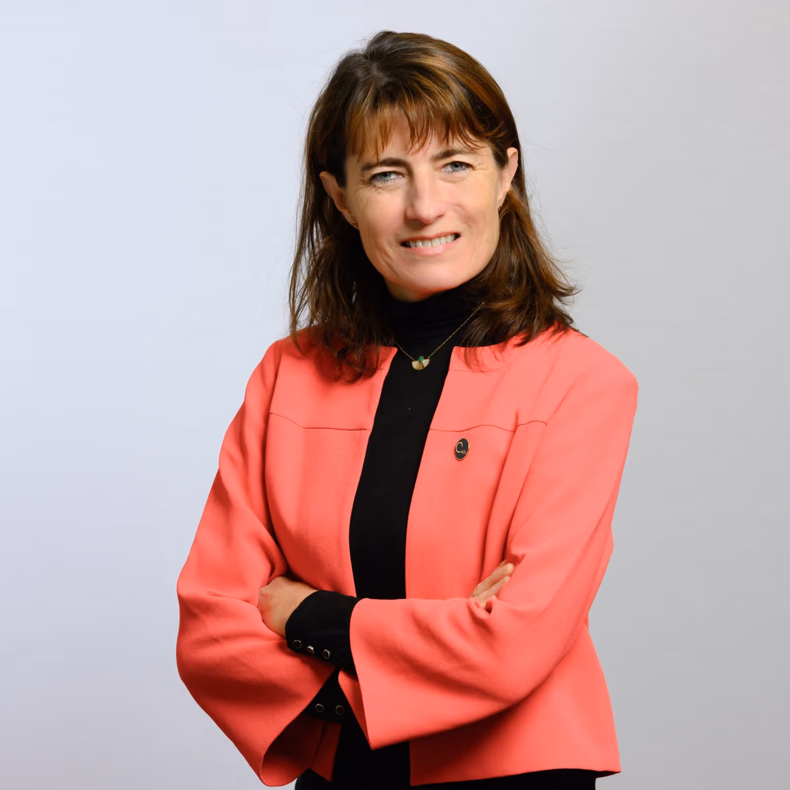 Portrait professionnel d’une femme souriante en veste corail, bras croisés sur fond clair.

Portrait d’un homme en costume foncé et lunettes