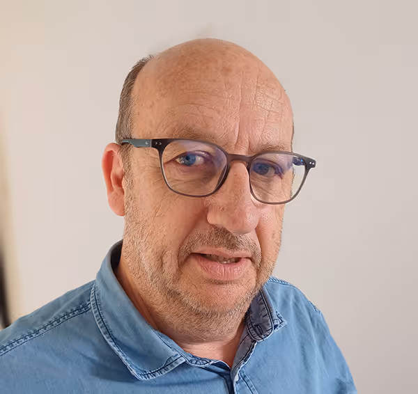 Portrait d’un homme portant des lunettes et une chemise en jean, regardant vers l’objectif sur fond clair.