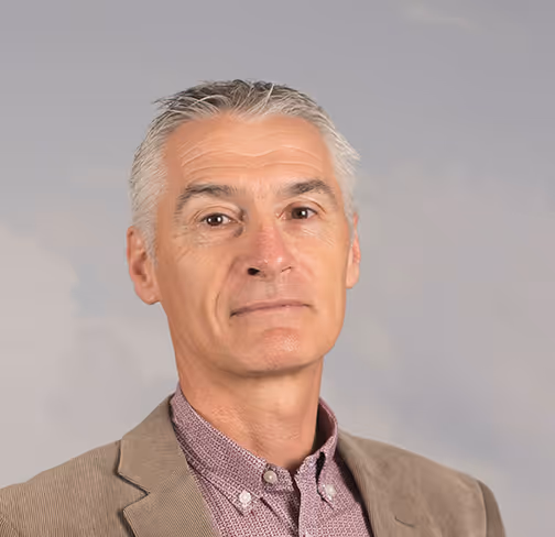 Balise alt [WEB] a dit :Portrait d’un homme aux cheveux gris, vêtu d’une veste beige et d’une chemise à motifs, posé devant un fond neutre. Image destinée à illustrer un profil professionnel ou une présentation institutionnelle.