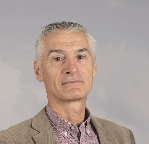 Balise alt [WEB] a dit :Portrait d’un homme aux cheveux gris, vêtu d’une veste beige et d’une chemise à motifs, posé devant un fond neutre. Image destinée à illustrer un profil professionnel ou une présentation institutionnelle.