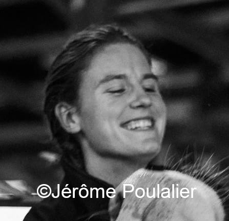 Femme souriante en tenue professionnelle, interagissant avec une vache en intérieur, ambiance conviviale en noir et blanc.