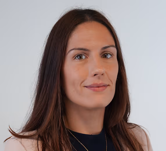 Portrait en buste d’une femme en tenue professionnelle, veste beige et haut bleu marine, posant sur fond clair, utilisé dans un contexte institutionnel ou de présentation d’équipe.