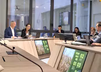 Réunion d'affaires autour d'une table avec plusieurs participants concentrés, écrans affichant des graphiques sur la production agricole.