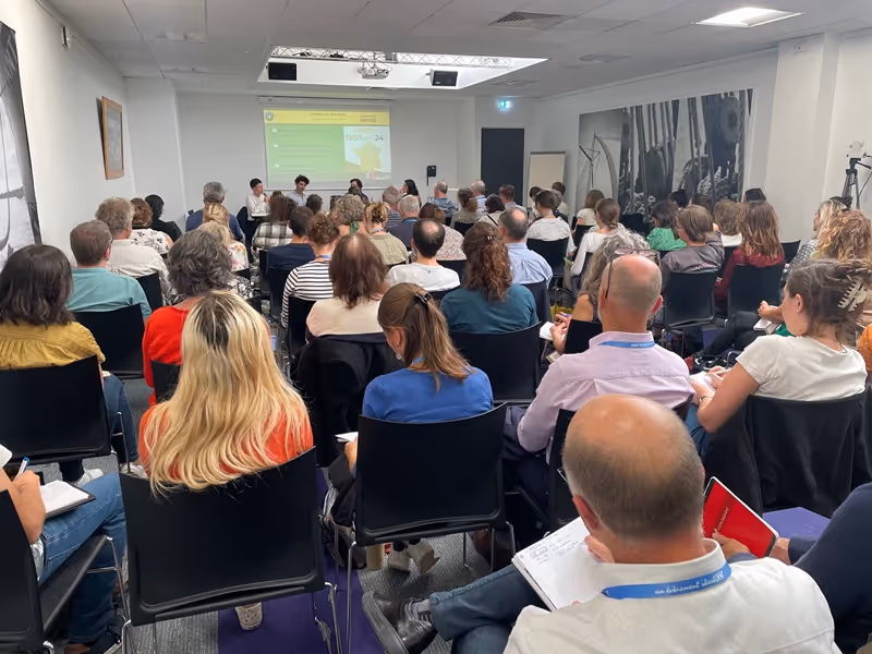 Homme âgé intervenant à un pupitre lors du Symposium Luzerne, avec une pancarte indiquant "Le 8 février 2024, Châlons-en-Champagne