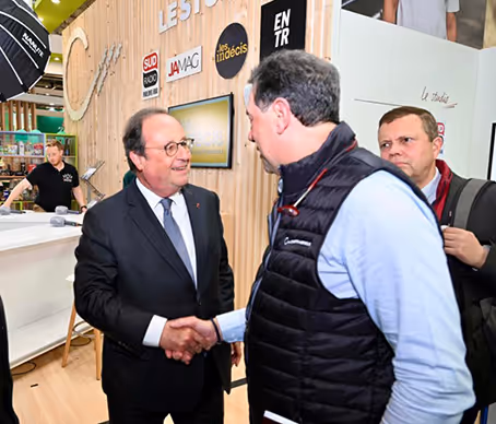 Poignée de main entre un homme politique en costume et un professionnel du secteur, lors d’un salon ou d’un événement viticole.