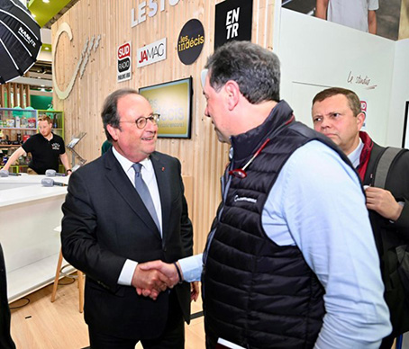 Poignée de main entre un homme politique en costume et un professionnel du secteur, lors d’un salon ou d’un événement viticole.