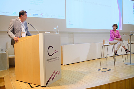 Conférence sur la coopération agricole avec un intervenant à la tribune et une intervenante assise sur scène.