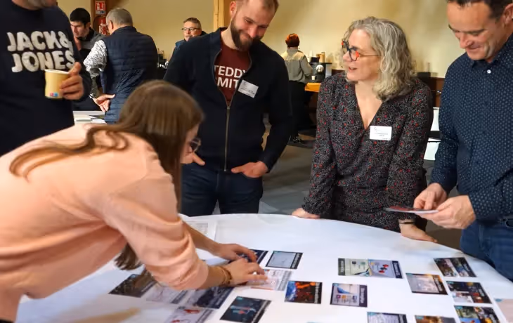 Groupe de personnes échangeant autour d’une table circulaire couverte de cartes lors d’un atelier collaboratif, dans un cadre professionnel et convivial