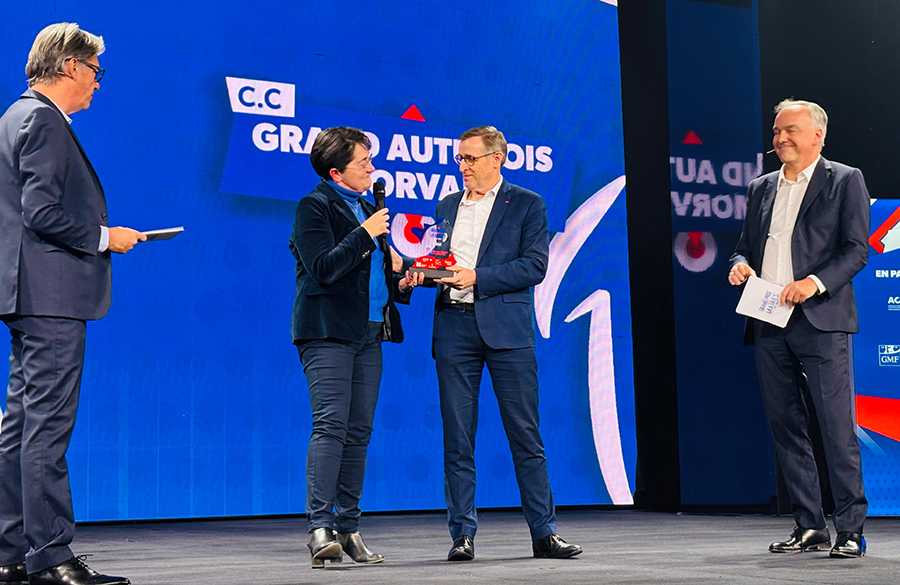 Remise de prix sur scène lors du Grand Prix des Maires 2025, avec quatre personnes en costume, dont une femme remettant un trophée à un lauréat, sur fond d’écran bleu affichant le nom de la communauté de communes « Grand Autunois Morvan ».