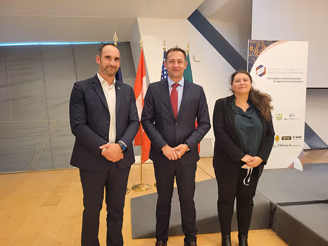 Photo officielle lors d’une conférence agricole internationale, avec trois intervenants posant devant les drapeaux de plusieurs pays et un kakémono de l'événement.