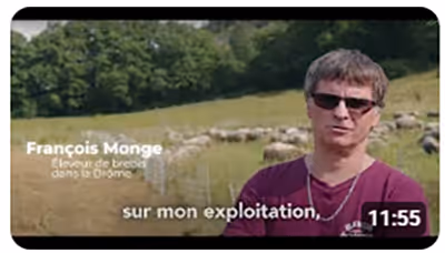 Capture d’écran d’une vidéo témoignage de François Monge, éleveur de brebis dans la Drôme, parlant de son exploitation agricole avec un troupeau en arrière-plan.