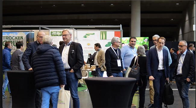 Professionnels en discussion dans les allées d’un salon international dédié aux filières agricoles et agroalimentaires, devant des stands de produits naturels et coopératifs.