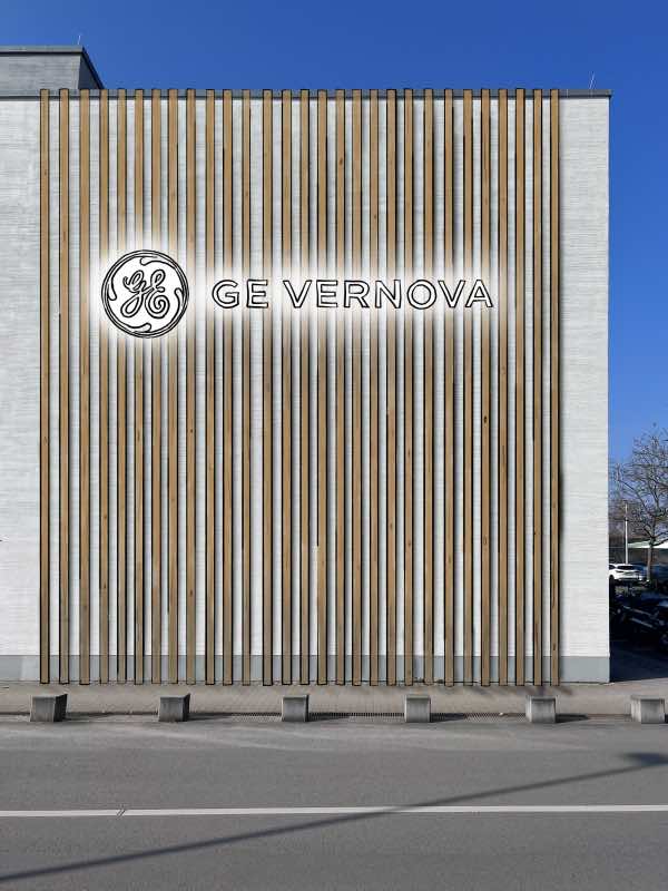 Gebäudefassade mit vertikalen Holzpaneelen und beleuchtetem GE Vernova Logo bei klarem Himmel.