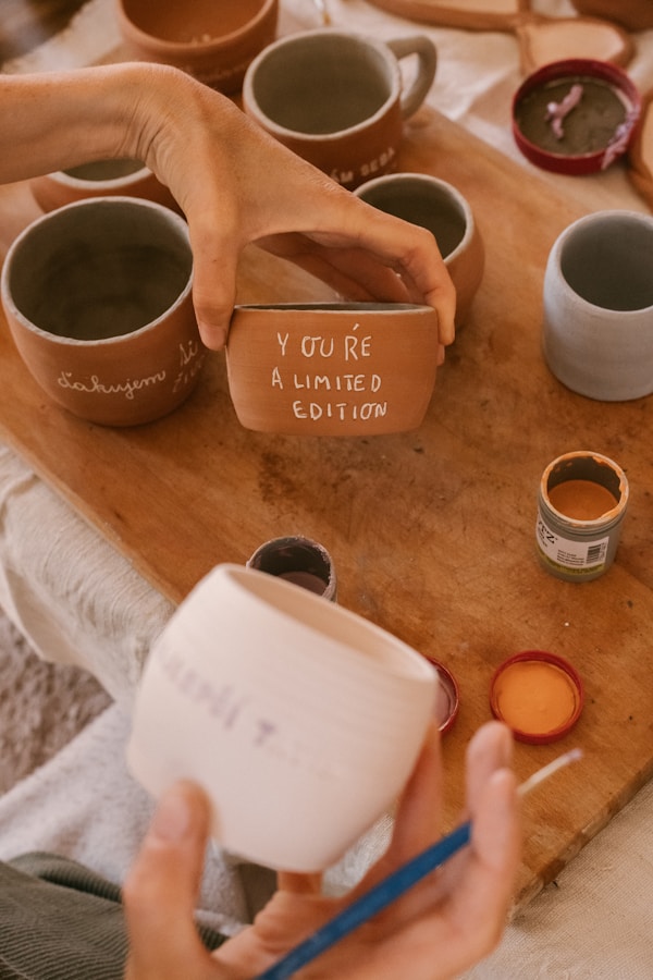 Potter hand paints a pot with words on a wooden table.