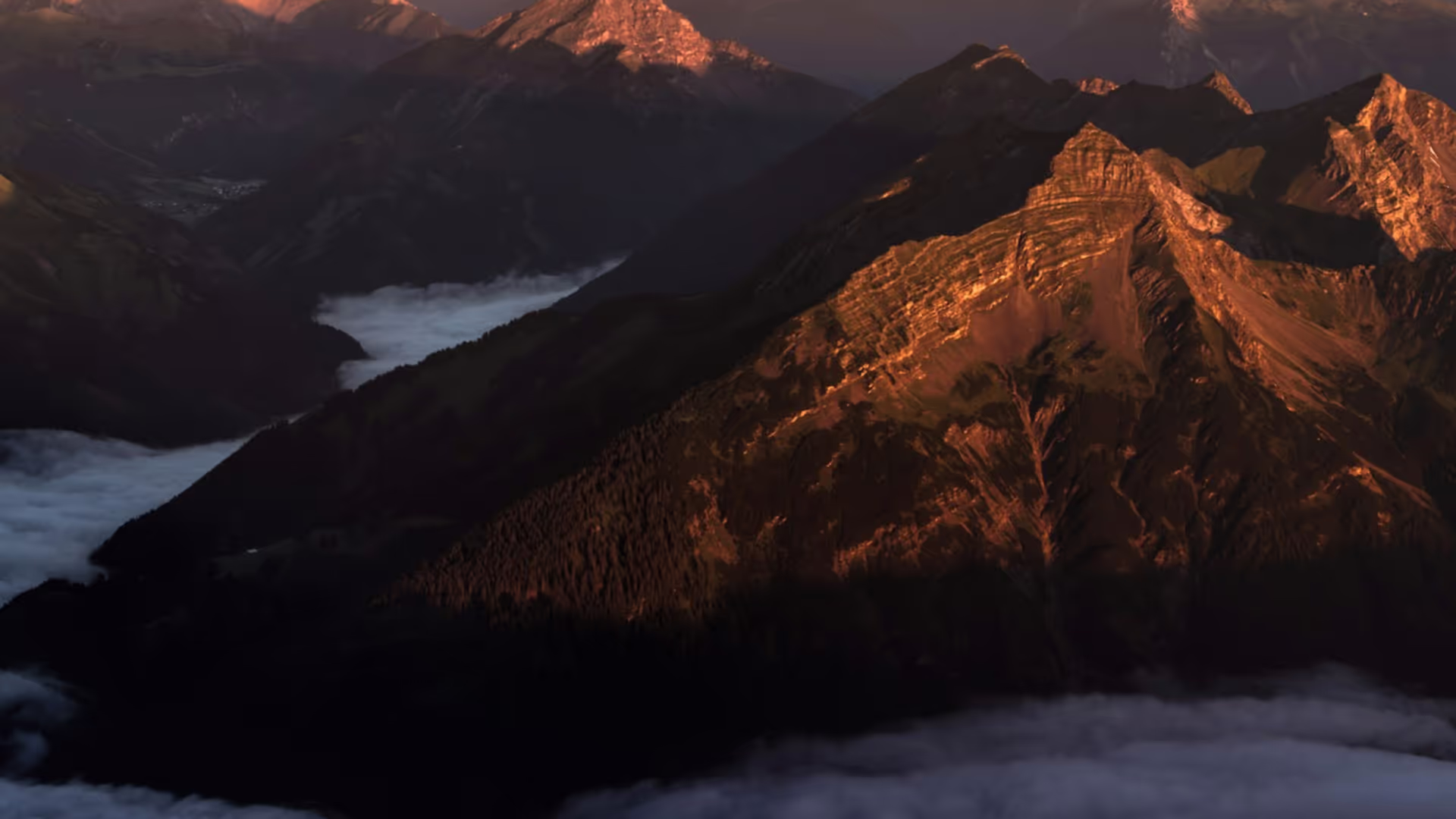 Mountain range with low lying clouds and the sun touching the peaks.